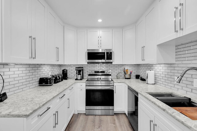 kitchen with sink, light stone countertops, white cabinets, and appliances with stainless steel finishes