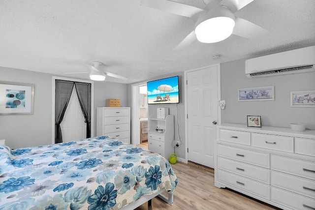 bedroom featuring ceiling fan, light wood-type flooring, a textured ceiling, and an AC wall unit