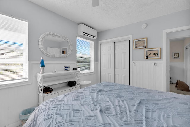 bedroom with ceiling fan, a wall mounted AC, a closet, and a textured ceiling