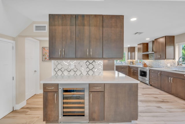 kitchen with stainless steel electric range, sink, beverage cooler, dark brown cabinetry, and wall chimney exhaust hood