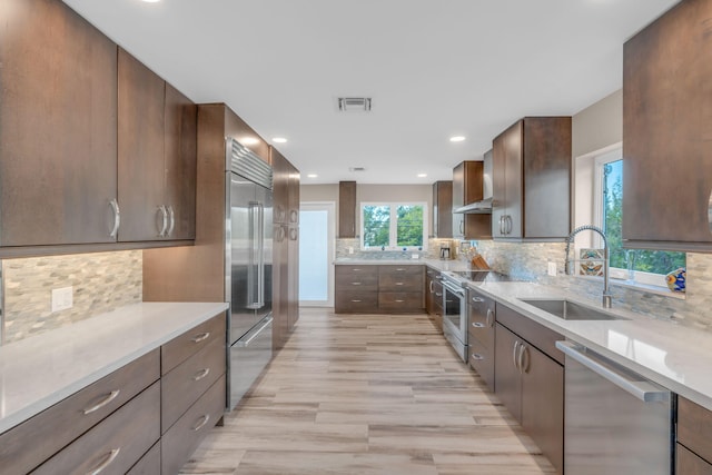 kitchen featuring wall chimney exhaust hood, sink, high end appliances, tasteful backsplash, and light stone countertops