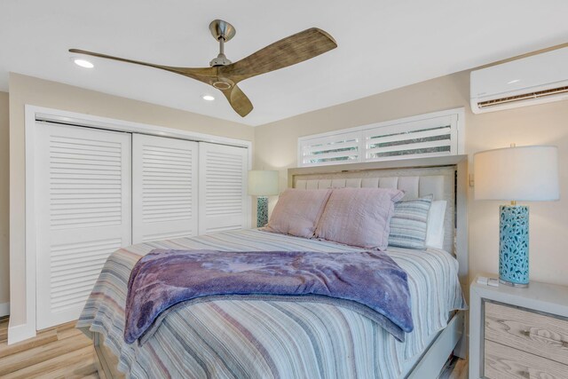 bedroom with a closet, light hardwood / wood-style floors, an AC wall unit, and ceiling fan