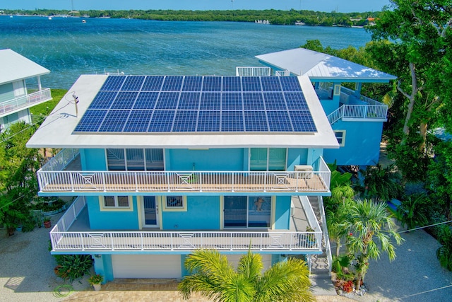 back of property with driveway, a garage, solar panels, a water view, and stucco siding