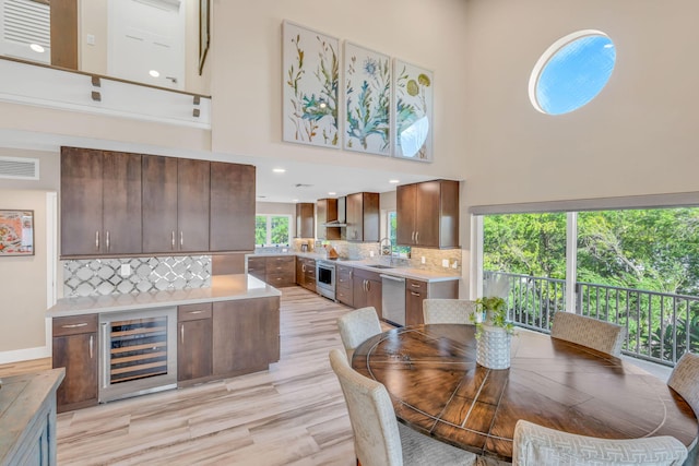 dining space with a high ceiling, light wood-style floors, wine cooler, and visible vents