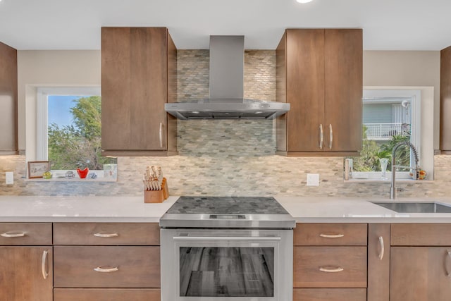 kitchen with wall chimney exhaust hood, stainless steel electric stove, light countertops, and a sink