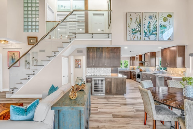 living area featuring a towering ceiling, light wood finished floors, wine cooler, and stairway