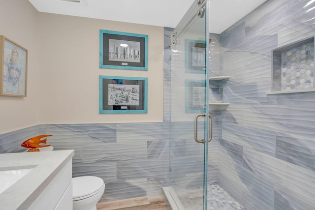 bathroom featuring vanity, a shower with shower door, tile walls, and toilet