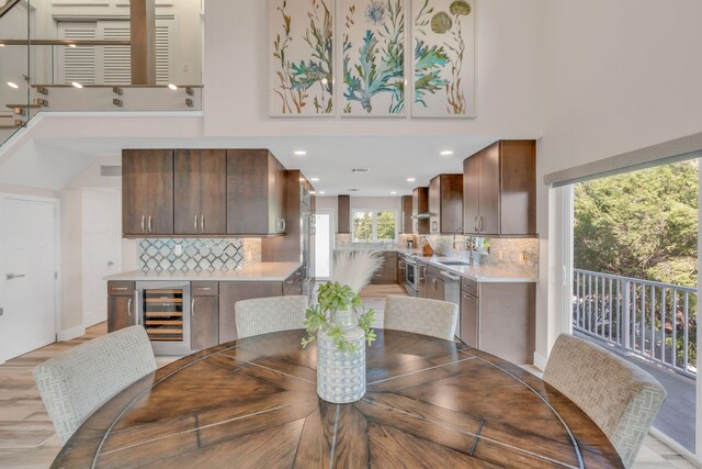 dining space featuring beverage cooler, light wood finished floors, visible vents, and a towering ceiling