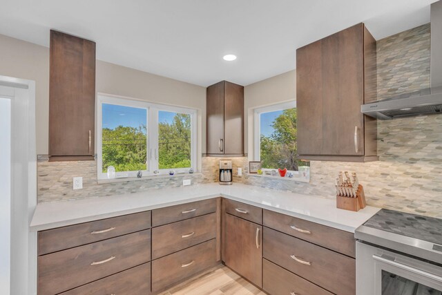 kitchen with dark brown cabinetry, light stone counters, electric stove, wall chimney range hood, and backsplash