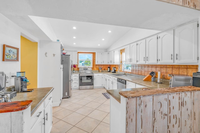 kitchen featuring a peninsula, light tile patterned floors, a sink, appliances with stainless steel finishes, and decorative backsplash