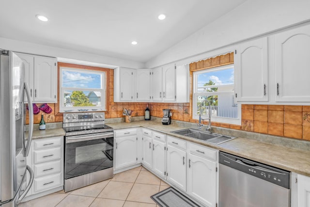 kitchen featuring a sink, stainless steel appliances, tasteful backsplash, vaulted ceiling, and white cabinets