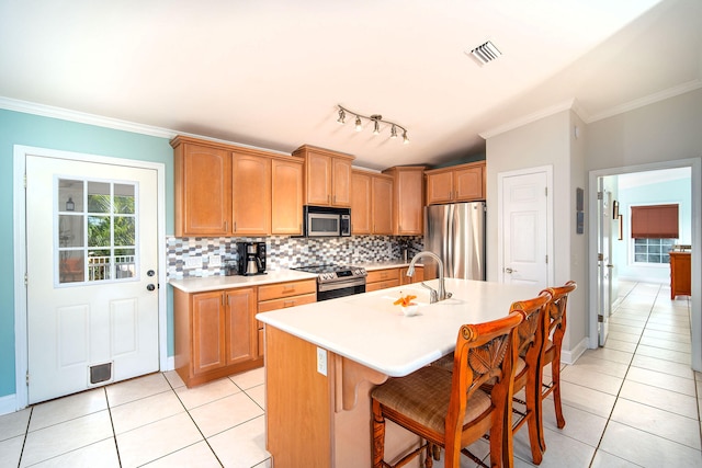 kitchen featuring sink, light tile patterned floors, appliances with stainless steel finishes, a kitchen breakfast bar, and an island with sink