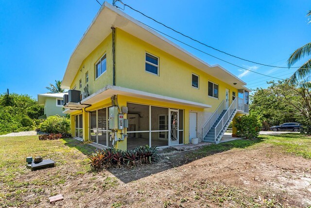 back of property with a sunroom, a yard, and central AC