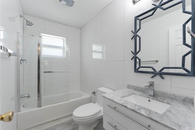 full bathroom featuring tiled shower / bath, tile walls, hardwood / wood-style flooring, vanity, and toilet