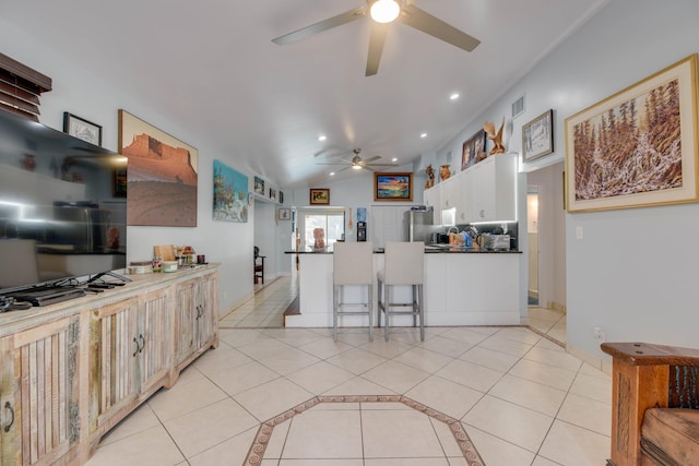 kitchen with light tile patterned floors, stainless steel refrigerator, ceiling fan, white cabinetry, and vaulted ceiling