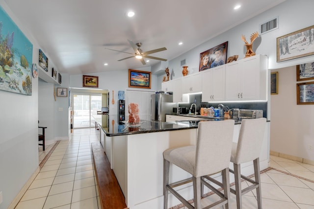 kitchen featuring light tile patterned flooring, vaulted ceiling, stainless steel fridge, white cabinets, and backsplash