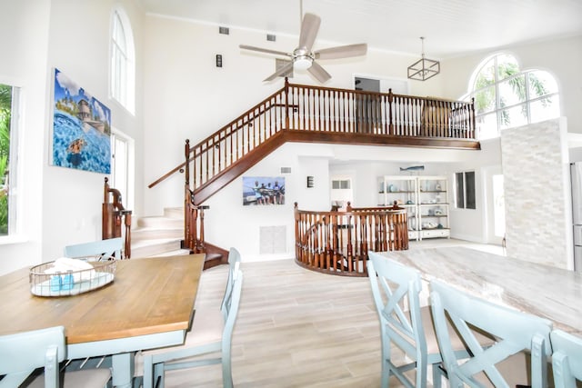 dining area featuring a ceiling fan, stairs, light wood finished floors, and a high ceiling