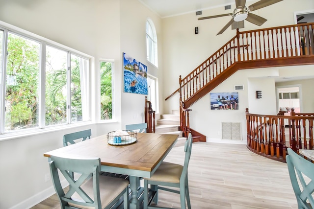dining space with light wood-type flooring, visible vents, ceiling fan, a high ceiling, and baseboards