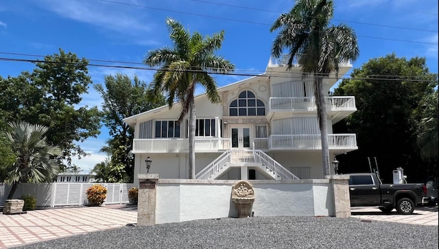 coastal inspired home with a balcony, french doors, a fenced front yard, stairs, and stucco siding