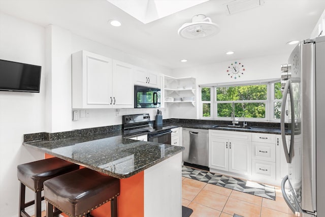 kitchen with a peninsula, a sink, visible vents, appliances with stainless steel finishes, and dark stone countertops