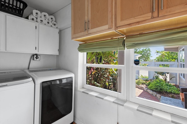 laundry area featuring a wealth of natural light, washing machine and clothes dryer, and cabinet space