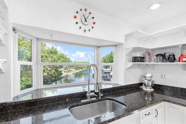 kitchen with open shelves, a water view, white cabinets, a sink, and dark stone countertops