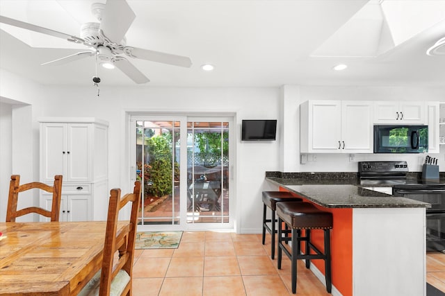 kitchen featuring light tile patterned floors, white cabinetry, a kitchen breakfast bar, black appliances, and dark stone countertops