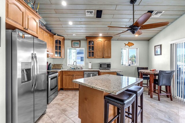 kitchen with a kitchen bar, sink, appliances with stainless steel finishes, a kitchen island, and light stone countertops