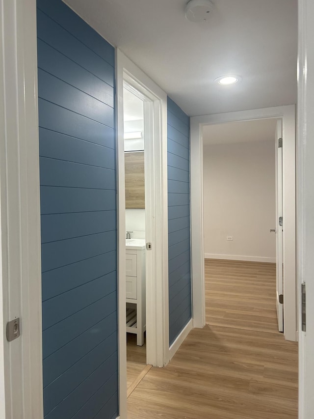 corridor featuring sink, light hardwood / wood-style flooring, and wooden walls