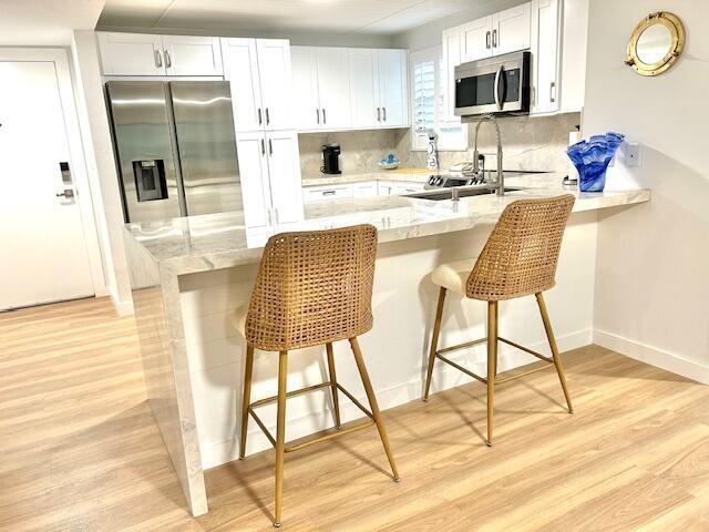 kitchen with appliances with stainless steel finishes, tasteful backsplash, white cabinets, a kitchen breakfast bar, and light hardwood / wood-style floors