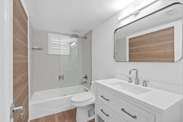 full bathroom with tiled shower / bath combo, vanity, hardwood / wood-style flooring, and toilet