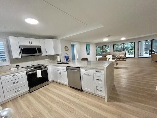 kitchen featuring appliances with stainless steel finishes, kitchen peninsula, light hardwood / wood-style floors, and white cabinets