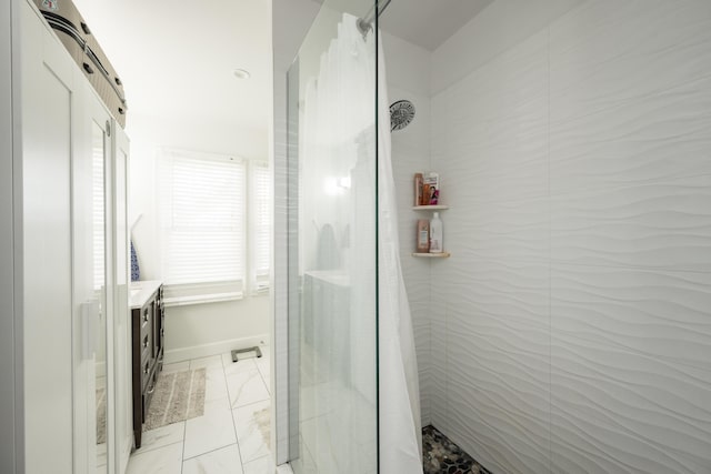 bathroom with marble finish floor, a tile shower, vanity, and baseboards