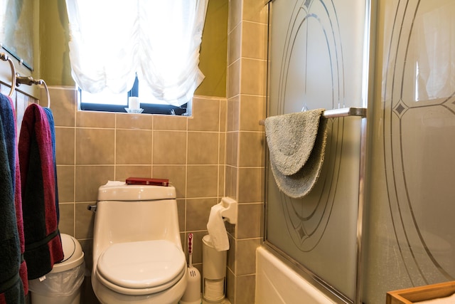 bathroom featuring enclosed tub / shower combo, toilet, and tile walls