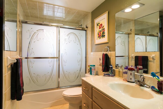 full bathroom featuring tile walls, bath / shower combo with glass door, vanity, tile patterned floors, and toilet