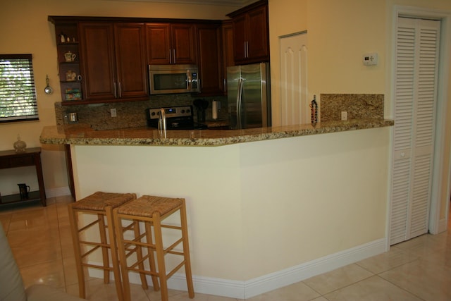 kitchen featuring appliances with stainless steel finishes, a breakfast bar, tasteful backsplash, kitchen peninsula, and light stone countertops