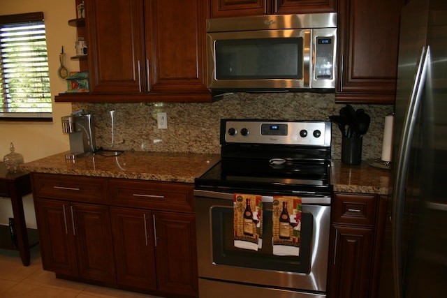 kitchen with light stone countertops, appliances with stainless steel finishes, light tile patterned floors, and backsplash