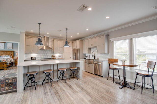 kitchen with appliances with stainless steel finishes, wall chimney exhaust hood, a center island, and hanging light fixtures