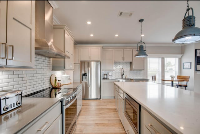 kitchen featuring appliances with stainless steel finishes, decorative light fixtures, sink, crown molding, and wall chimney range hood