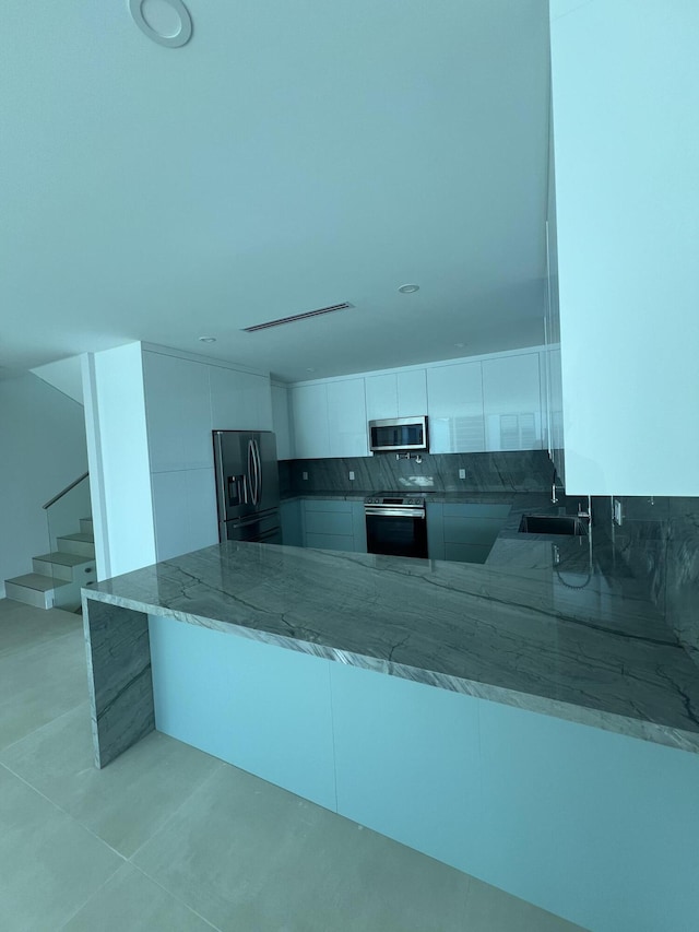 kitchen featuring sink, light stone counters, kitchen peninsula, stainless steel appliances, and white cabinets