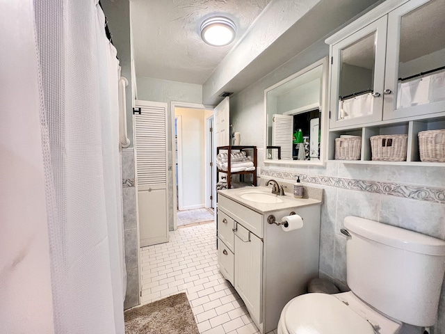 bathroom with tile walls, vanity, toilet, tile patterned floors, and a textured ceiling