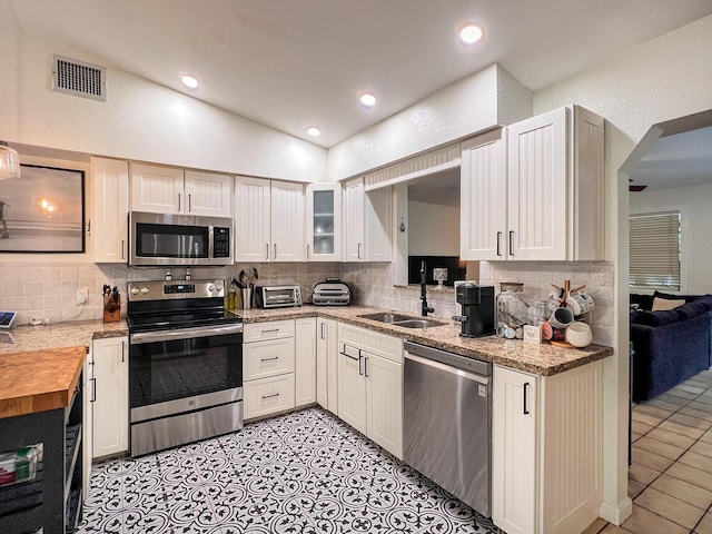 kitchen featuring lofted ceiling, sink, stainless steel appliances, and white cabinets