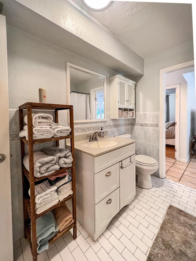 bathroom with tile patterned floors, toilet, tile walls, a textured ceiling, and vanity