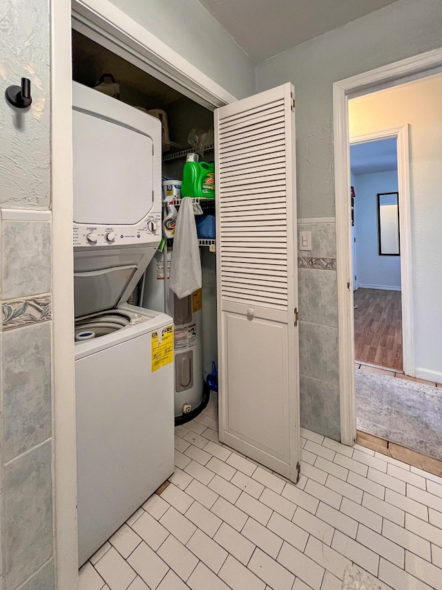 laundry area featuring tile walls, water heater, and stacked washer / dryer