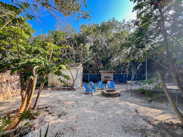 view of yard with a trampoline, exterior fireplace, a shed, and an outdoor fire pit