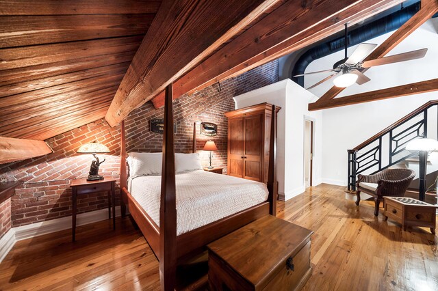 bedroom featuring high vaulted ceiling, light wood-type flooring, ceiling fan, brick wall, and beam ceiling