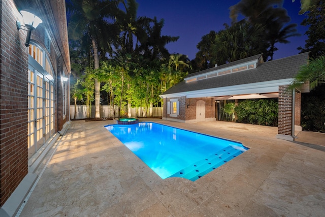 pool at night featuring a patio and an outbuilding