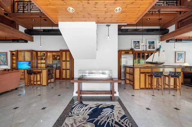 kitchen with a kitchen bar, built in refrigerator, hanging light fixtures, a high ceiling, and wooden ceiling