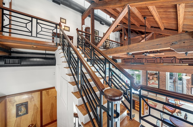 stairs with hardwood / wood-style flooring, wooden ceiling, a high ceiling, and beamed ceiling