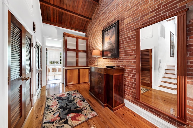 hall featuring vaulted ceiling with beams, wood ceiling, brick wall, and light wood-type flooring